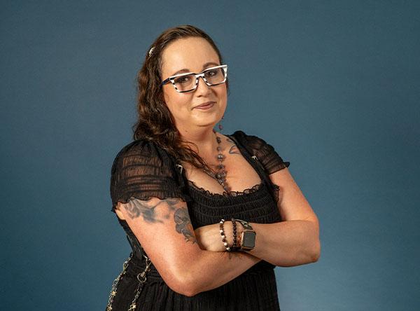 a woman with glasses in all black standing with her arms crossed