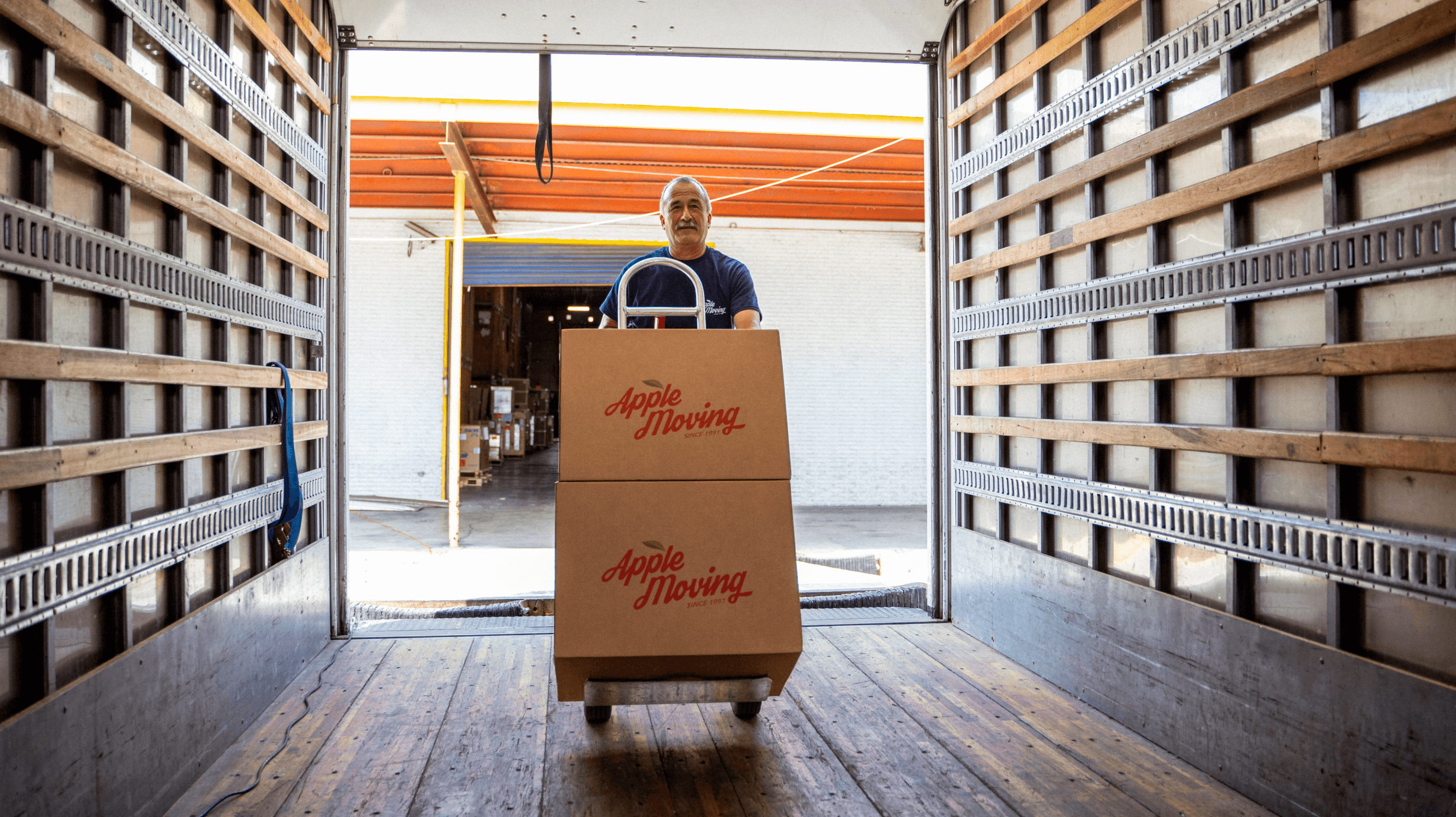 An Apple Moving employee pushing a dolly of branded boxes inside a moving truck.