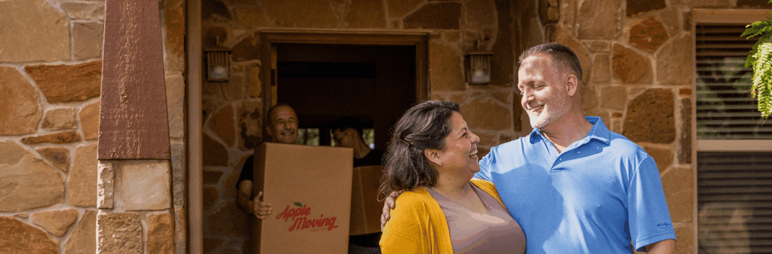 A couple smiling at each other while Apple Moving employees move boxes out of their home.