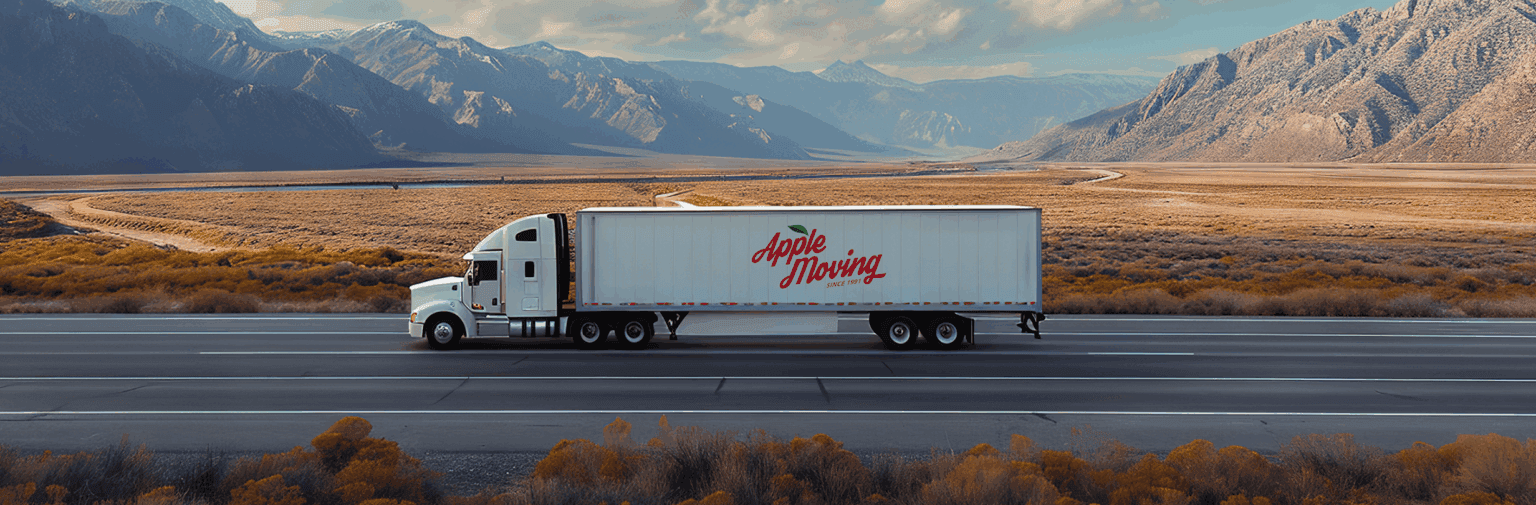 An Apple Moving truck driving on an open road with mountains in the distance.