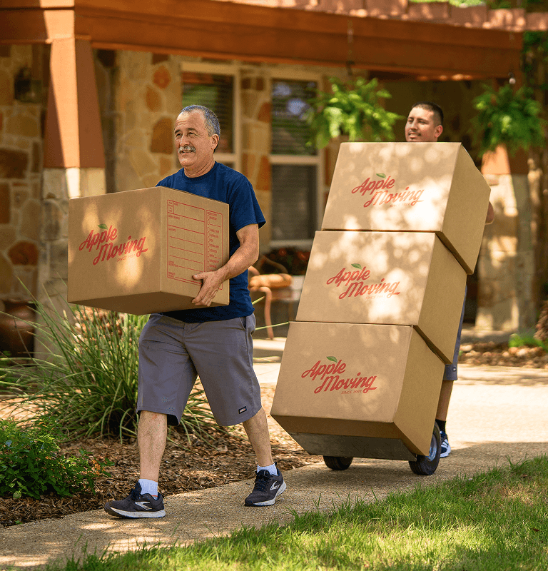 Two Apple Moving employees transporting boxes out of a house.