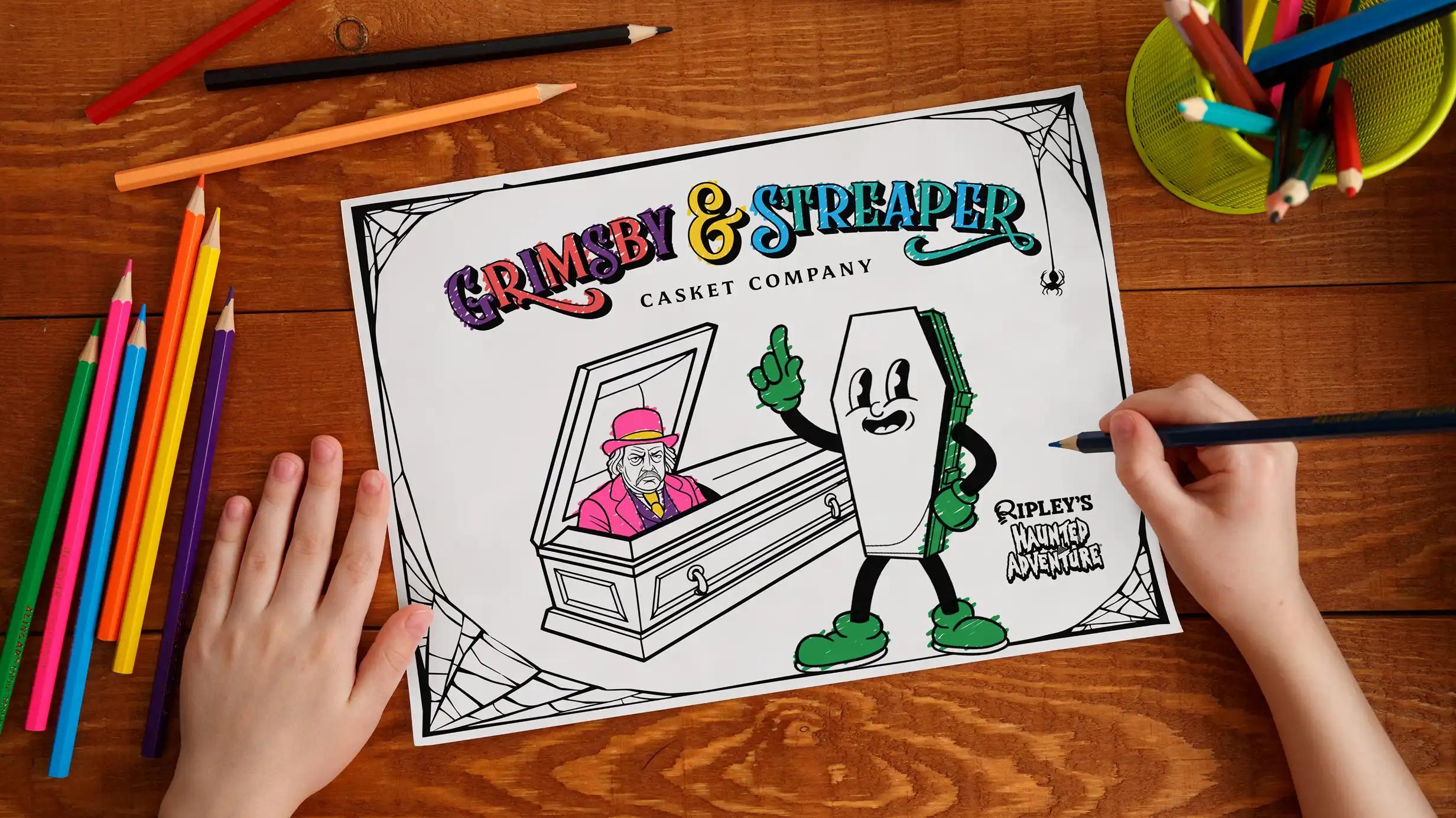 Child coloring a Grimsby & Streaper Casket Company activity sheet featuring a cartoon coffin character and a grumpy man in a casket, surrounded by colored pencils on a wooden table.