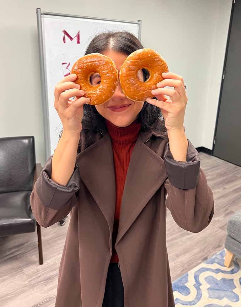 A woman playfully holding two doughnuts up to her eyes